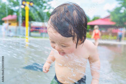 Happy toddler boy playing in water park spray ground