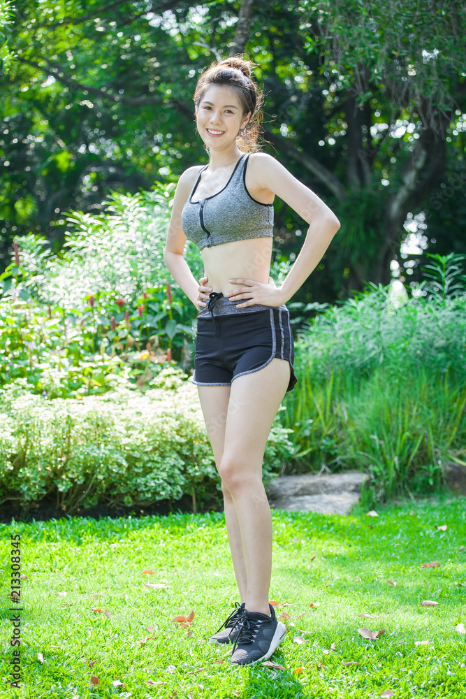 Asian Sport young woman slim fitness in sports bra smiling and standing  hands on hips in park exercise workout and running in sport wear. Healthy  lifestyle and fashion concepts. Stock Photo