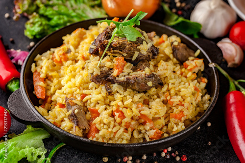Uzbek Oriental cuisine. Pilaf in a cast-iron frying pan made of lamb. next to the vegetables on a black table.