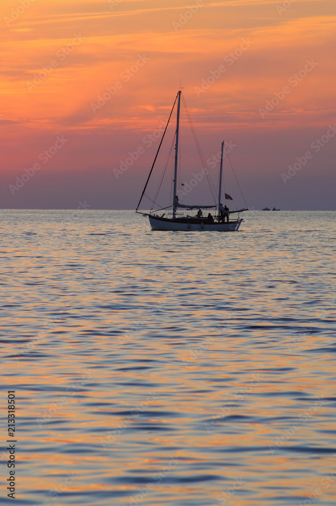 Beautiful sunset over sea with reflection and silhouette of small boat