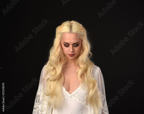 close up portrait of a blonde girl wearing white lace gown. black studio background.