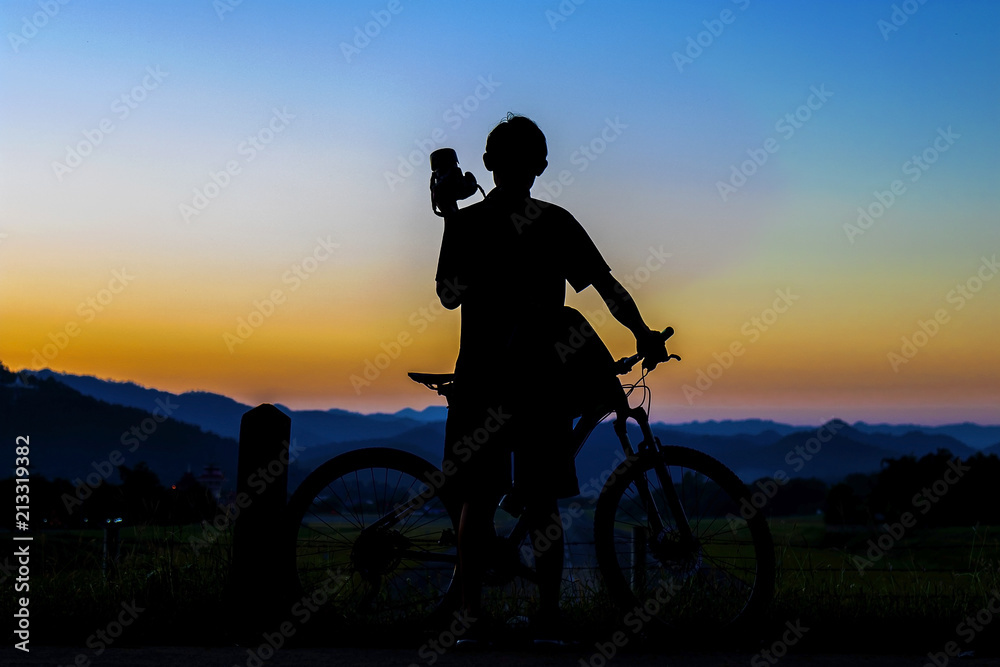 Obraz premium Silhouette of photographer in action take photo with bike on mountain with sunrise.