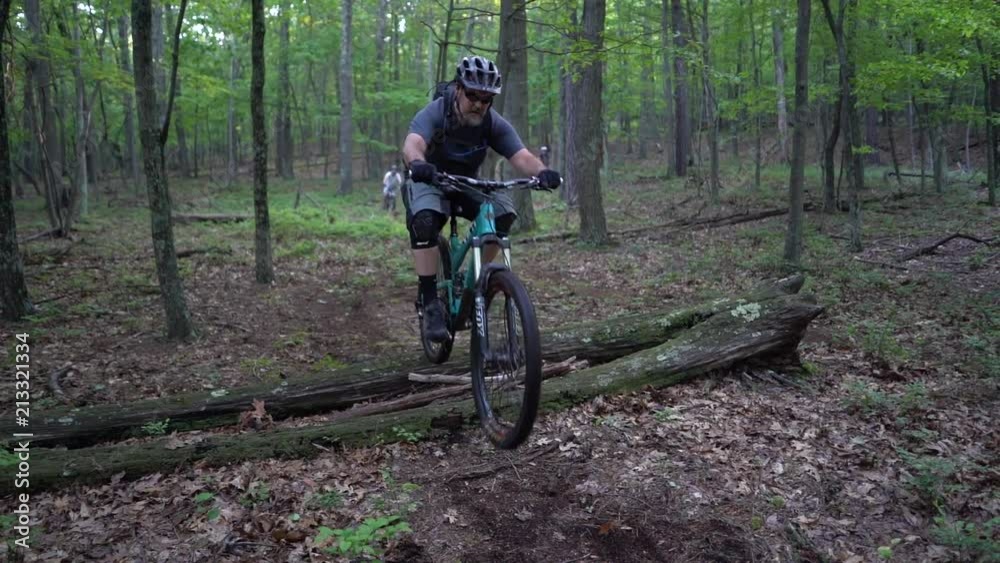 Closeup of mountain bikers jumping over a log in a forest single track. Closeup of mountain bikers jumping over a log in a forest single track.