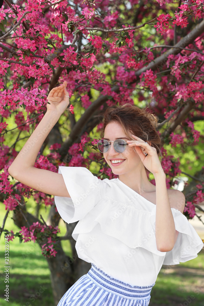 Attractive young woman posing near blossoming tree on sunny spring day
