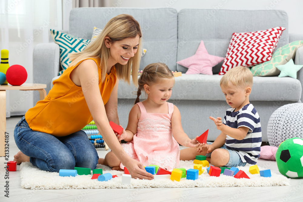Fototapeta premium Young woman and cute children playing with constructor on floor at home
