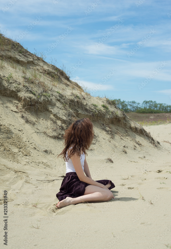 Woman in a skirt sits on the sand in the nature