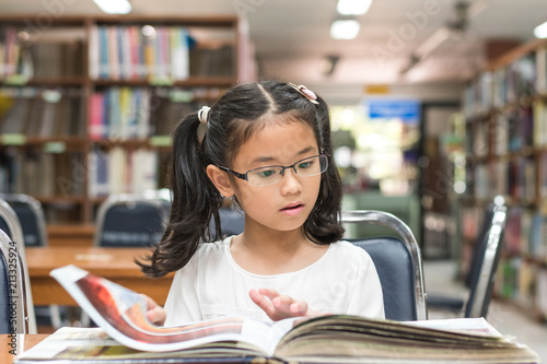 School education and literacy concept with Asian girl kid student learning and reading book in library or classroom