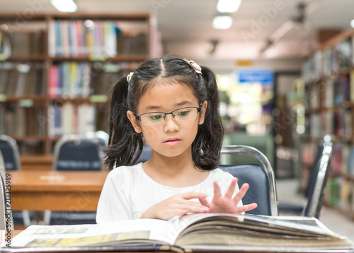 School education and literacy concept with Asian girl kid student learning and reading book in library or classroom