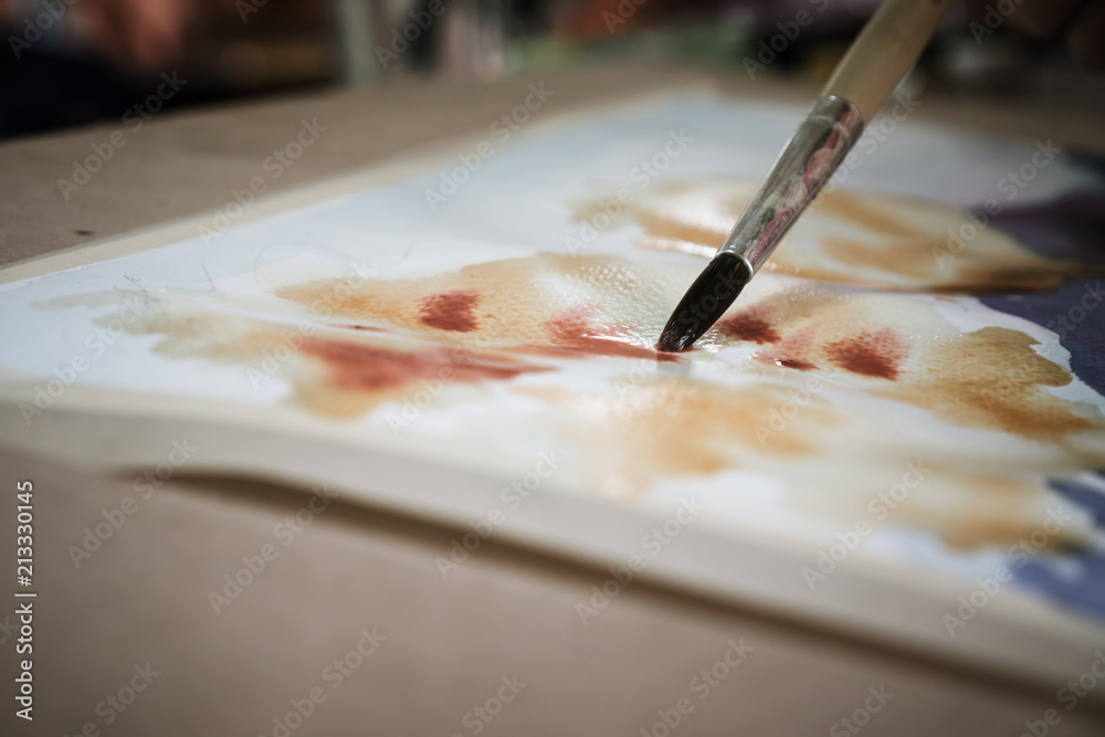 Fototapeta premium Student's hand with brush drawing on paper for creation picture abstract of watercolor painting with bamboo brush in Art subject classroom secondary education in Thailand