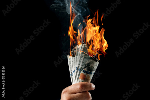 Male hand close-up, holds burning money in hands, burning US dollars. Black background, isolate. The concept of inflation, a decrease in the purchase of foreign currency, and devolution. photo