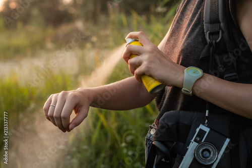 Woman using anti mosquito spray outdoors at hiking trip. Close-up of young female backpacker tourist applying bug spray on hands
