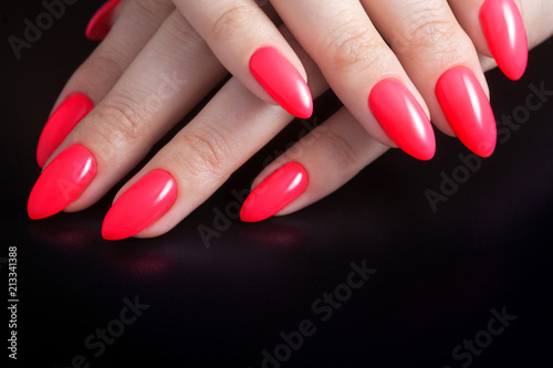 Women's hands with perfect red manicure. Nail Polish red coral color. Black background