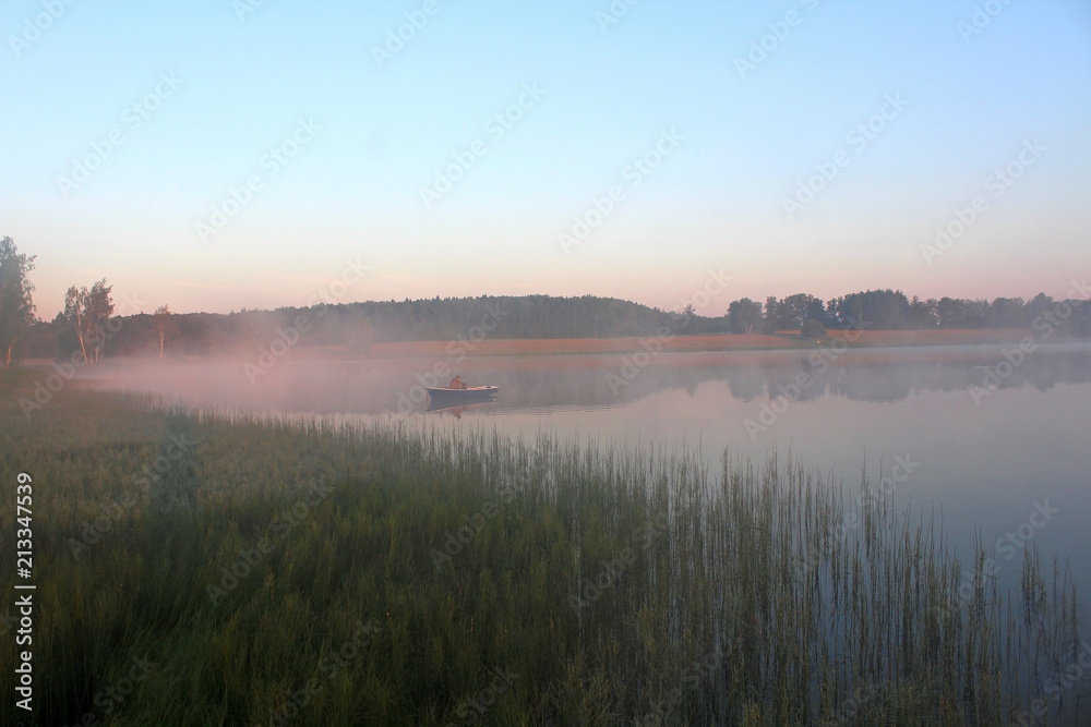 Beautiful summer nature on a pond in July. Fishermen in boats in the pre-dawn mist, in the rays of the walking sun.