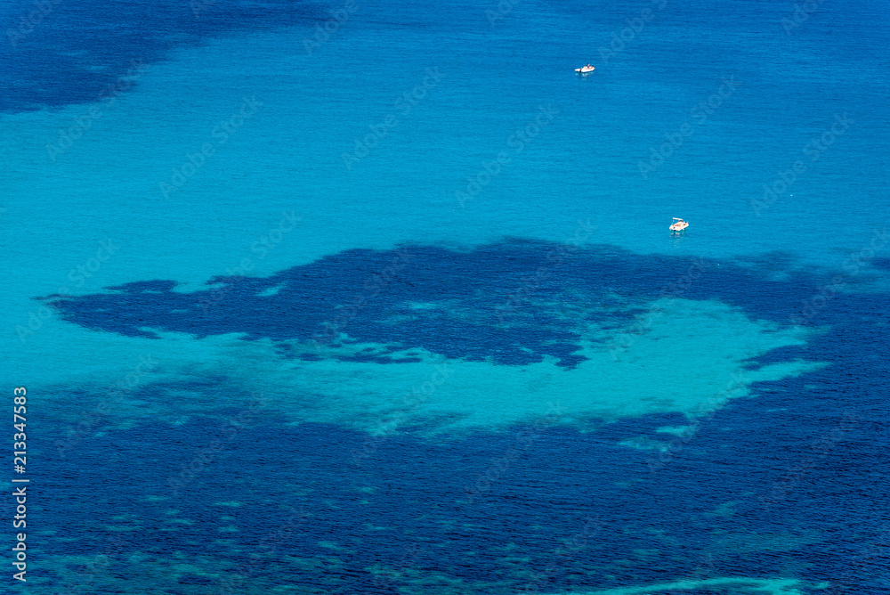 Aerial view of tropical turquoise blue sea with floating boats and people. High resolution image of sailing boats anchored next to reef around the coastline. Bird's eye view, ocean from above.