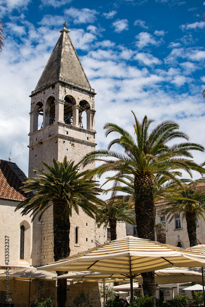 Historical building in the center of the city that is an island, where you can see the umbrellas on the terraces of the restaurants to rest. Photograph taken in Trogir, Croatia.