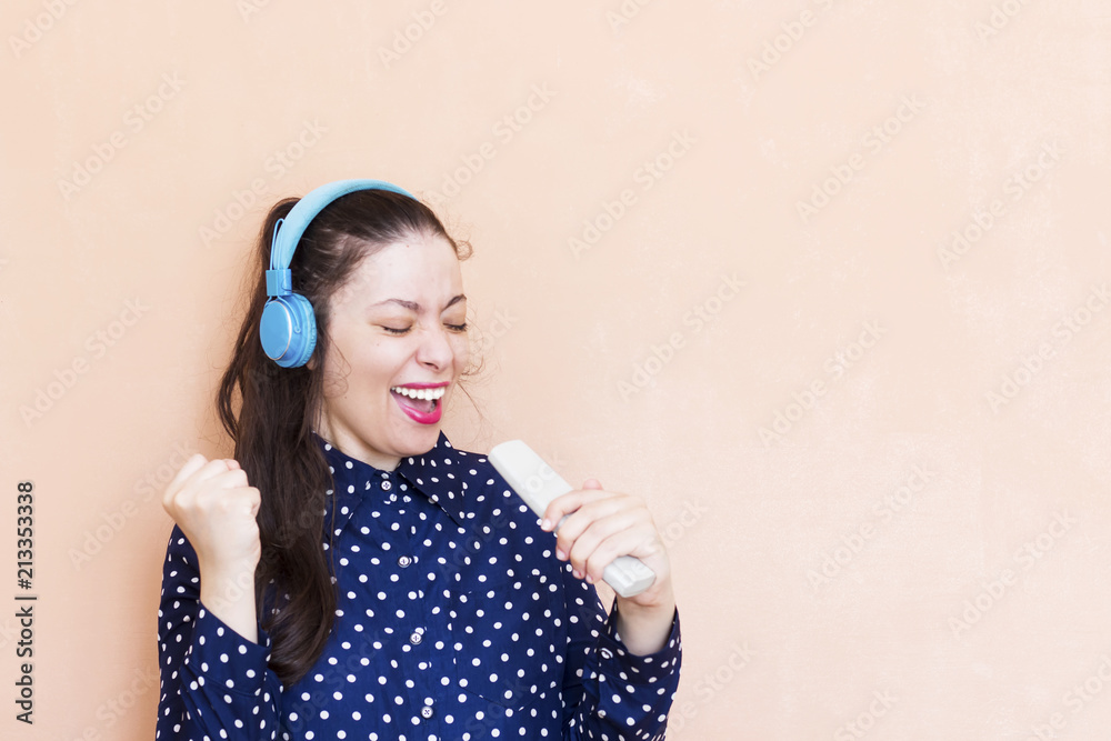 beautiful arab girl wearing blue t-shirt she singing, holding a remote control tv and listening to music with wireless earphones isolated over orange wall beautiful arab girl wearing blue t-shirt she singing, holding a remote control tv and listening to music with wireless earphones isolated over orange wall