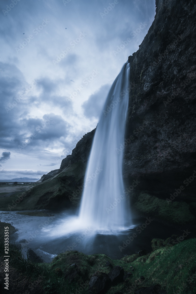 A wild natural fresh sparkling waterfall in a lonely green valley with moos covered rocks and ice cold mountain water flowing down black rocky walls on a rainy moody day in Iceland without tourists A wild natural fresh sparkling waterfall in a lonely green valley with moos covered rocks and ice cold mountain water flowing down black rocky walls on a rainy moody day in Iceland without tourists