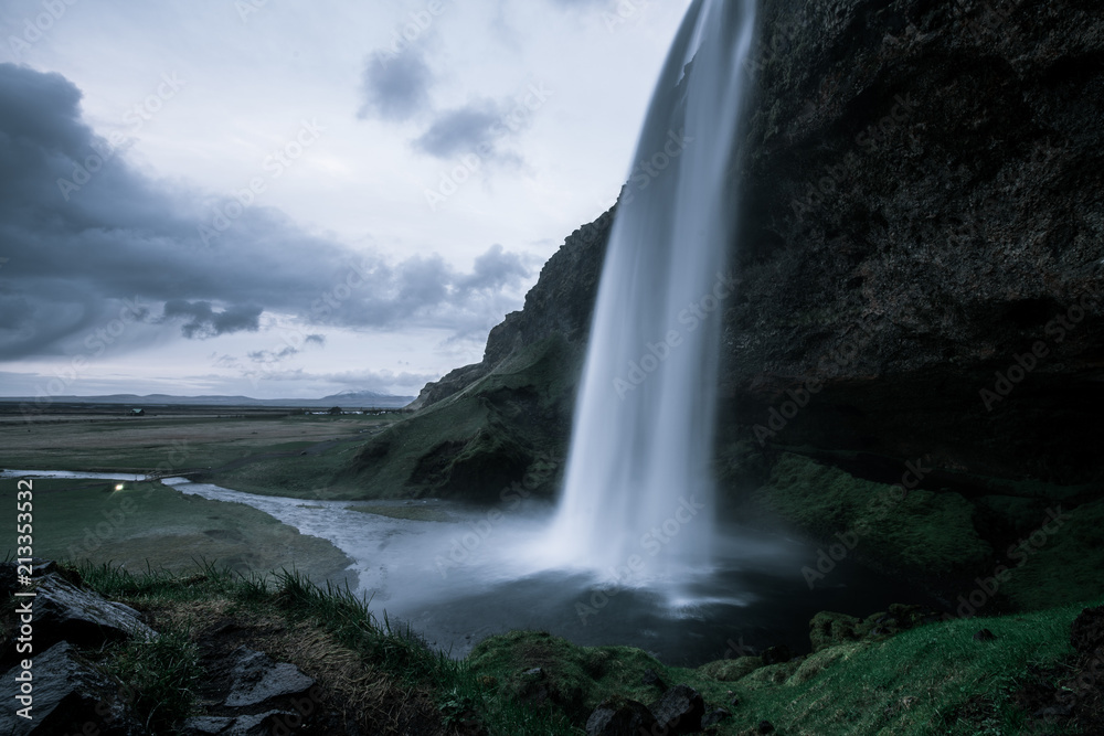 A wild natural fresh sparkling waterfall in a lonely green valley with moos covered rocks and ice cold mountain water flowing down black rocky walls on a rainy moody day in Iceland without tourists A wild natural fresh sparkling waterfall in a lonely green valley with moos covered rocks and ice cold mountain water flowing down black rocky walls on a rainy moody day in Iceland without tourists