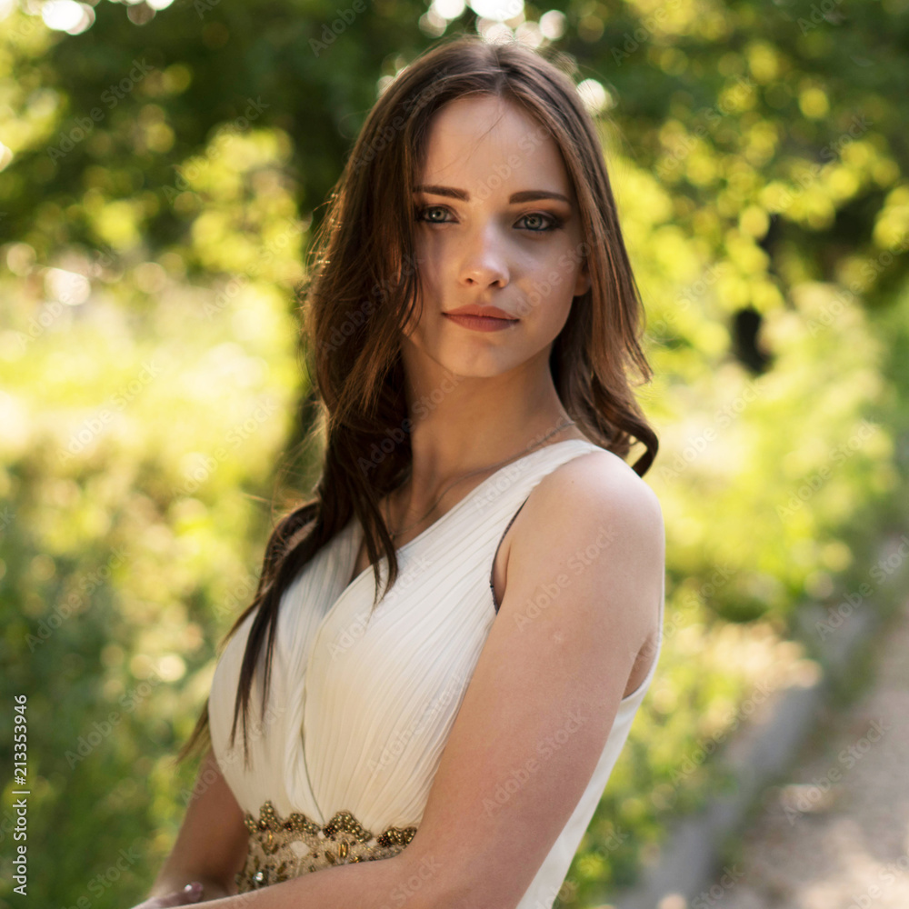 Summer portrait of young beautiful lady wearing long white evening dress posing in the park. Summer portrait of young beautiful lady wearing long white evening dress posing in the park.