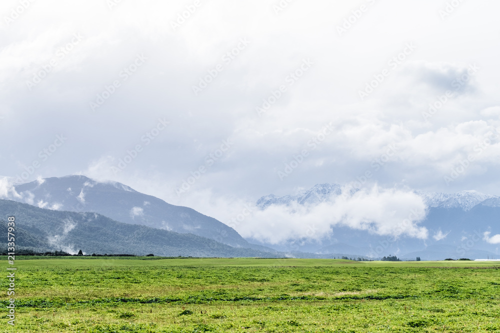 Beautiful landscape of a green meadows and snow mountain in a cloudy day. Foggy over the mountains.