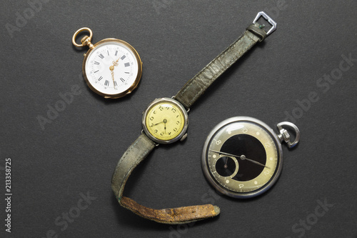 Set of watches on black background with a classic gold pocket watch a black and silver pocket watch and a wristwatch with worn leather straps