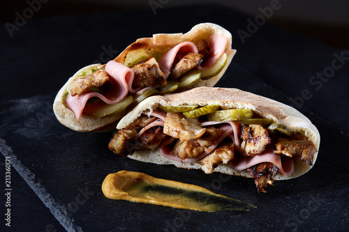 Stuffed pita bread with grilled vegetables, pork chops and sauce on black stony background, vertical.