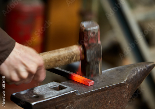 Close-up of a blacksmith's hands manipulating a metal piece above his forge, selective focus.