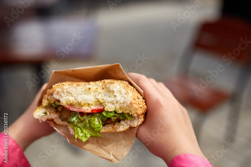 First person view shot of a girl eating hamburger in the street cafe, soft focus, shallow depth of field.
