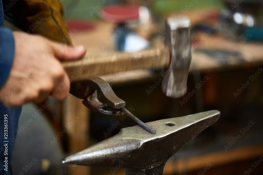 Close-up of a blacksmith's hands manipulating a metal piece above his forge, selective focus. Close-up of a blacksmith's hands manipulating a metal piece above his forge, selective focus.