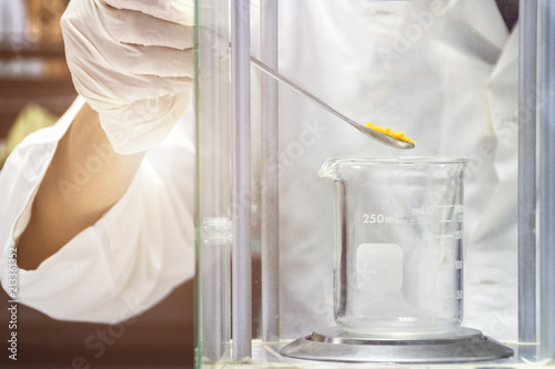 close up of hand wear glove is pouring sample to beaker to weighting on electronic balance in chemical laboratory