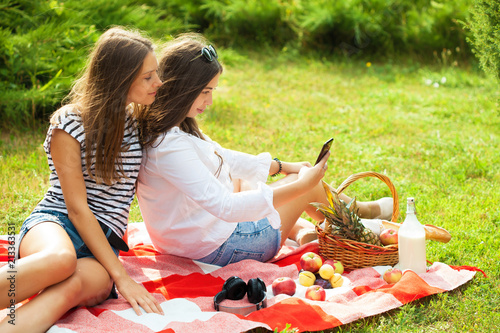 Two beautiful young women on a picnic looking at the smartphone screen photo