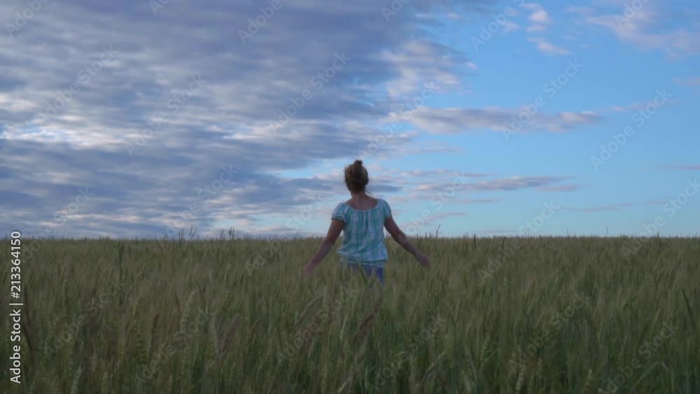 The girl runs through the field of young wheat unripe.
