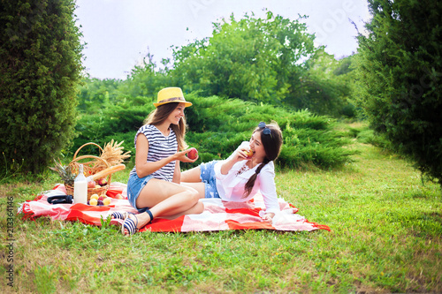 Two beautiful young girls at a summer picnic eating apples