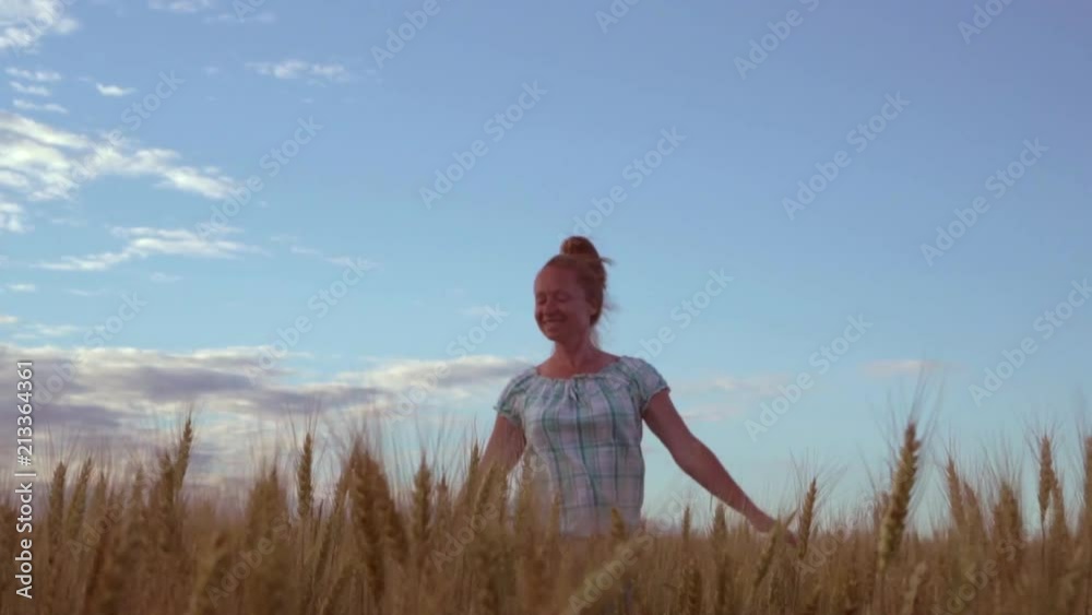 A happy girl with a smile on her face is walking on the field with wheat during sunset.
A happy girl with a smile on her face is walking on the field with wheat during sunset.