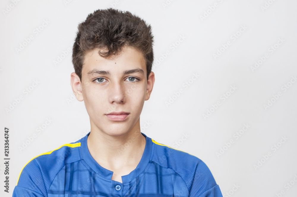 Portrait of a young guy in a blue T-shirt on a gray background. He has a serious but kind look Portrait of a young guy in a blue T-shirt on a gray background. He has a serious but kind look