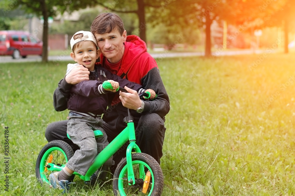 The father hugs a little son. Son and father rest after father taught his son to ride on a balanced bicycle