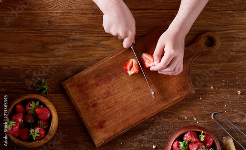 Knife in girl's hand cutting a fresh strawberry on wooden table, top view, selctive focus. photo