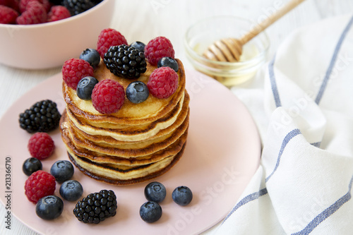 Pancakes with berries and honey on a round pink plate, low angle. Closeup.