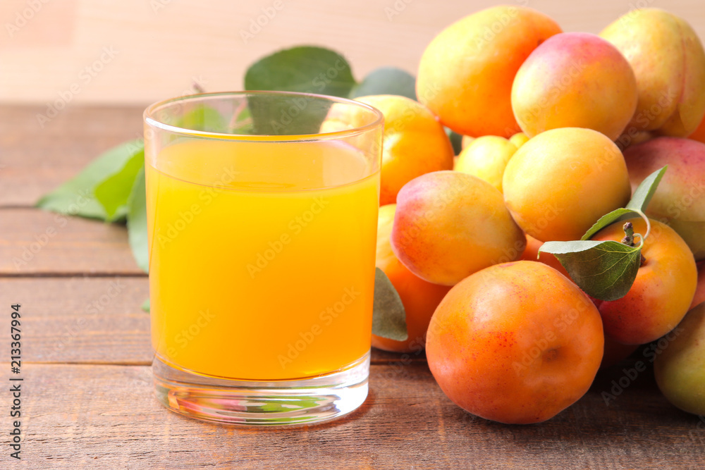 Apricot juice in a glass cup next to fresh apricots on a brown wooden background