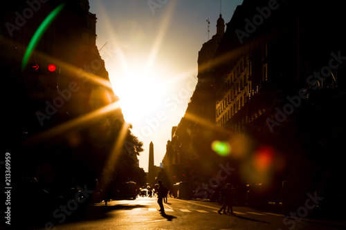 Tela Avenue with solar backlight, people walking and obelisk of Buenos Aires in the b