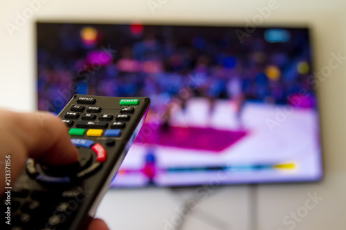 Close-up macro of man's hand with TV remote control watching a basketball game