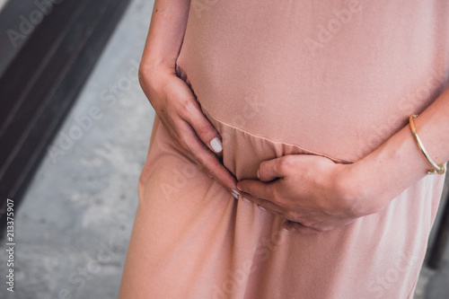 Young woman's in blush pink dress, hands on belly. Woman's health, menstruation, pregnancy, expecting a child concept