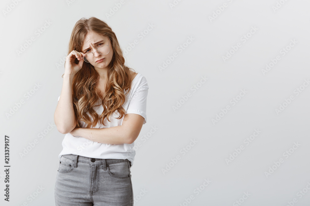 Girl is crying from misfortune. Upset gloomy attractive girlfriend with blond hair, taking off glasses, frowning and feeling unwell, crying or whining after offence or insult over gray background Girl is crying from misfortune. Upset gloomy attractive girlfriend with blond hair, taking off glasses, frowning and feeling unwell, crying or whining after offence or insult over gray background