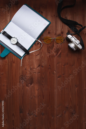 Layout of traveler, lifestyle concept. Diary clock and camera on textured wooden background