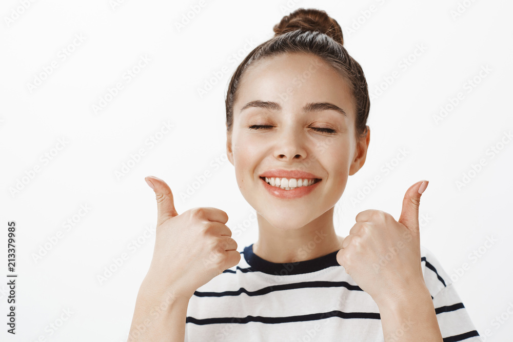 Female customer expressing her like of cosmetological procedure. Portrait of satisfied relaxed attractive woman with bun hairstyle, showing thumbs up and smiling broadly, feeling great and happy Female customer expressing her like of cosmetological procedure. Portrait of satisfied relaxed attractive woman with bun hairstyle, showing thumbs up and smiling broadly, feeling great and happy