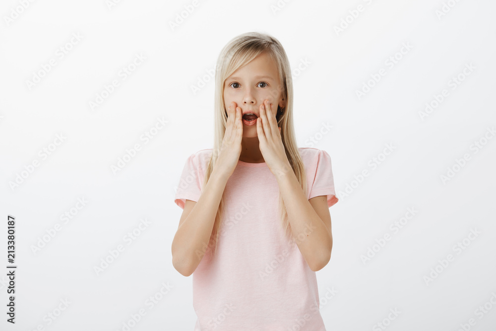 Portrait of curious serious girl with blond hair, holding palms near opened mouth and whispering, telling secret to friend, sharing important information, standing over gray background Portrait of curious serious girl with blond hair, holding palms near opened mouth and whispering, telling secret to friend, sharing important information, standing over gray background
