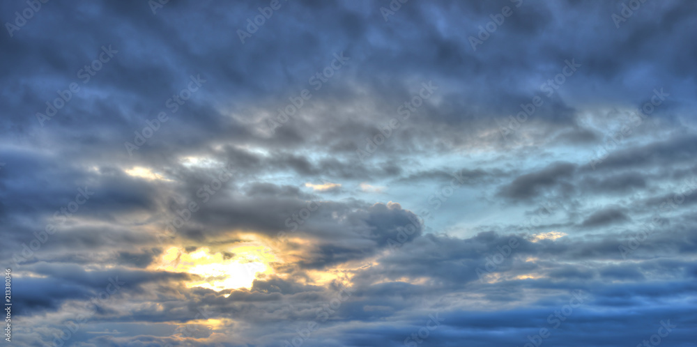 Cloudy, blue, rainy sky with clouds and sun. Colorful evening nature.