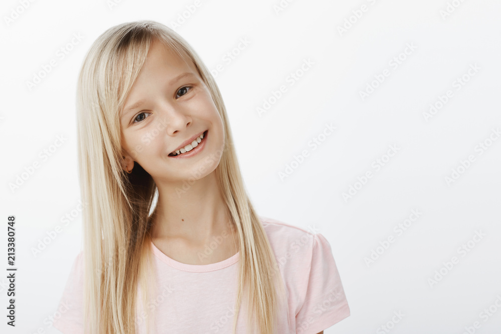 Waist-up shot of carefree joyful caucasian girl with blond hair, tilting head and smiling broadly, being satisfied and happy while talking with guy from school she likes, standing over gray wall Waist-up shot of carefree joyful caucasian girl with blond hair, tilting head and smiling broadly, being satisfied and happy while talking with guy from school she likes, standing over gray wall