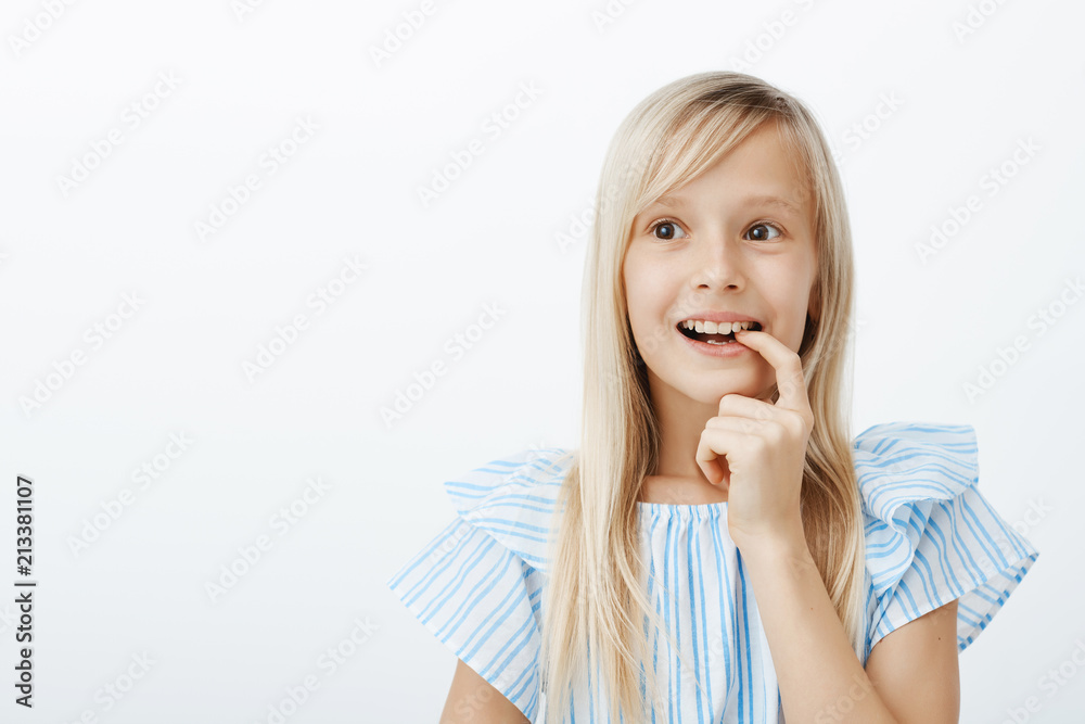 Charming creative young girl has great idea, deciding what to draw for mother birthday. Portrait of dreamy adorable child with blond hair, looking aside and biting finger with broad smile, imaging Charming creative young girl has great idea, deciding what to draw for mother birthday. Portrait of dreamy adorable child with blond hair, looking aside and biting finger with broad smile, imaging