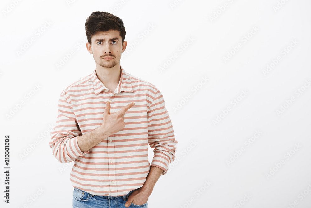 Not impressed with movie. Studio shot of indifferent uninterested caucasian male model with beard and moustache, holding hand in pocket and pointing at upper right corner with gloomy face Not impressed with movie. Studio shot of indifferent uninterested caucasian male model with beard and moustache, holding hand in pocket and pointing at upper right corner with gloomy face